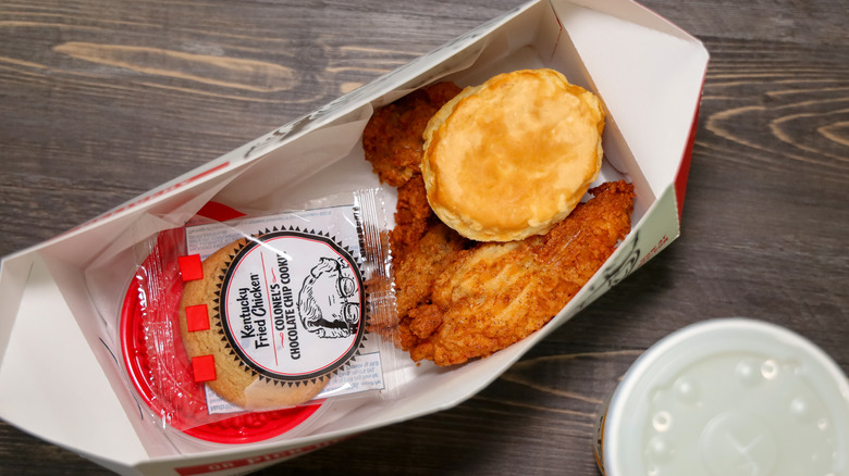  Top view of a KFC 2 piece chicken meal with a side, a biscuit and dessert inside a to fo box.