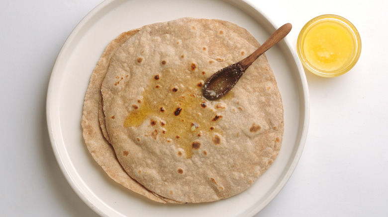 Ghee being spread with wooden spoon on roti bread