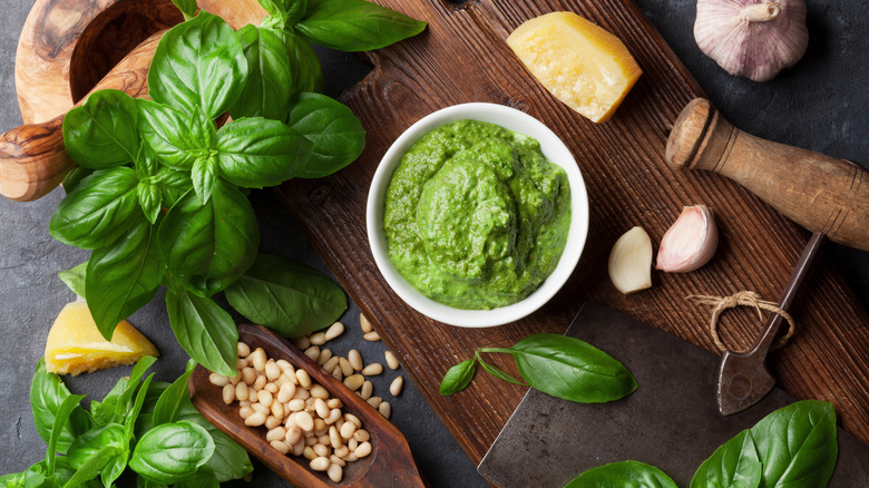 Pesto in a bowl with leaves of basil and parmesan cheese on a cutting board