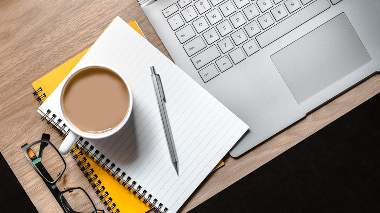 Cup of coffee alongside office supplies and laptop