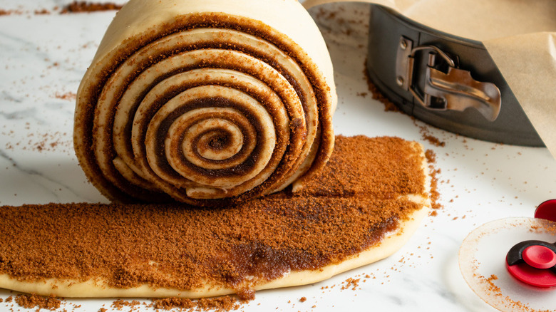 giant raw cinnamon roll on a counter being rolled up