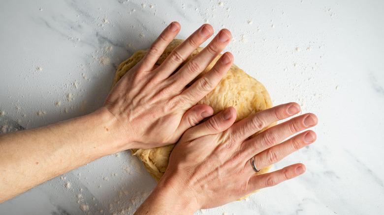 hands kneading dough on a floured countertop