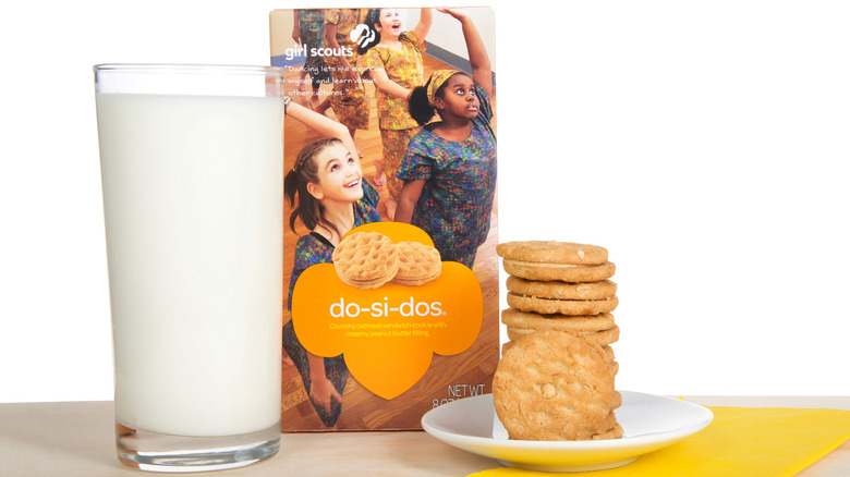 a box of do-si-dos next to a plate of girl scout cookies and a glass of milk