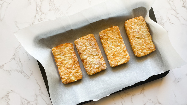 Four frozen hash browns on a parchment paper-lined baking pan