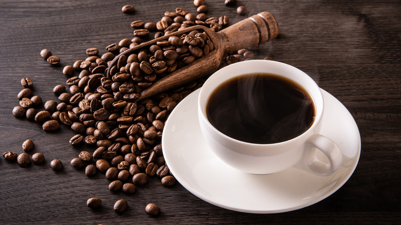 coffee beans in a shovel next to a cup of coffee. 