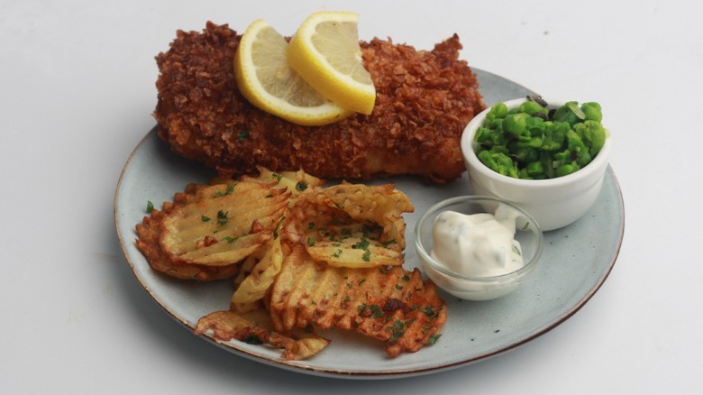 Plate of fried cod, waffle fries, and mushy peas with tartar sauce and lemon slices