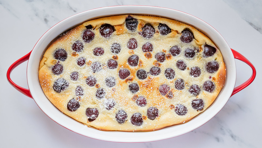 Clafoutis with cherries in red and white baking dish on stone counter