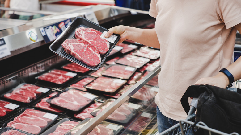 person holding package of meat in store