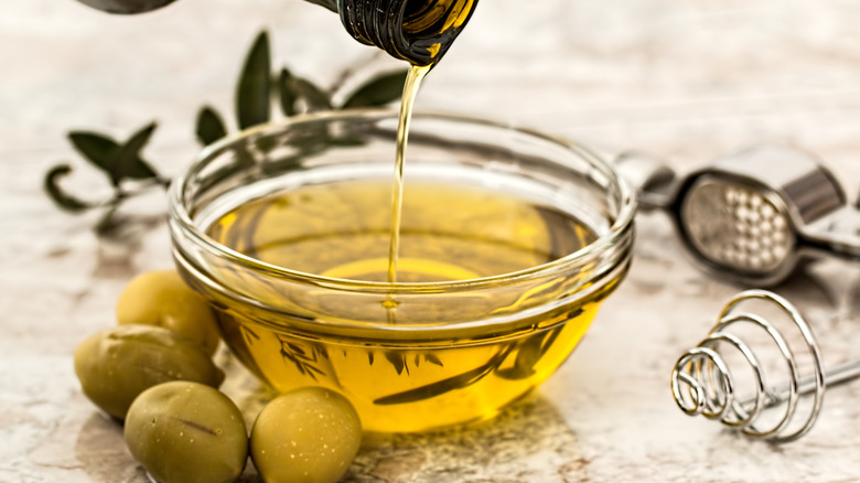 A glass bowl of olive oil with green olives next to it
