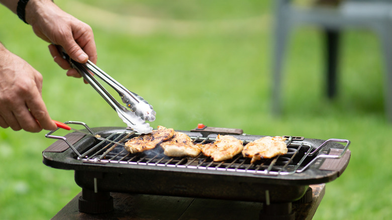 hands with tongs on grill