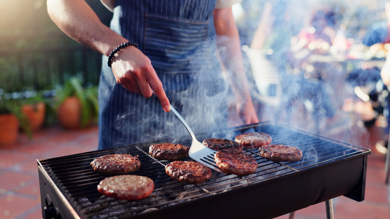 person cooking burgers on grill