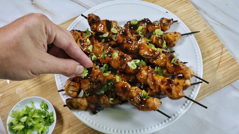 sprinkling scallions on chicken skewers