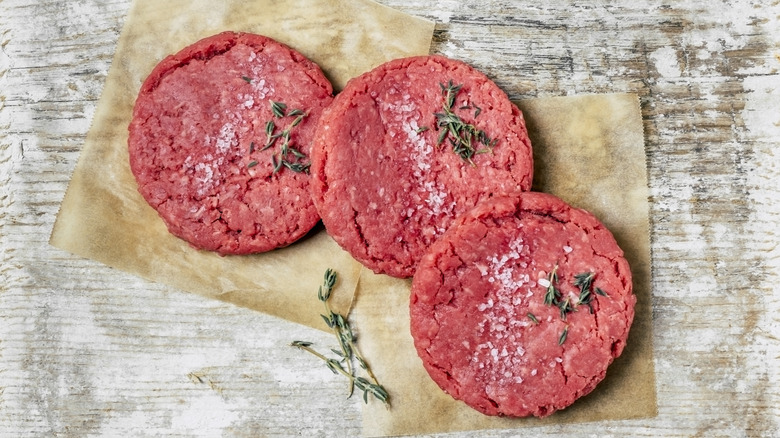 Three raw ground beef patties with salt