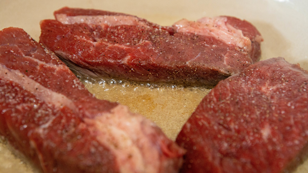 three steaks searing in hot oil for Guinness stew