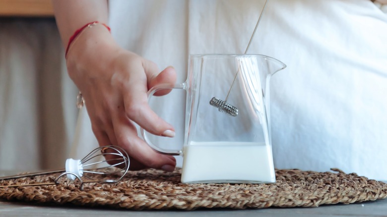 person using handheld milk frother