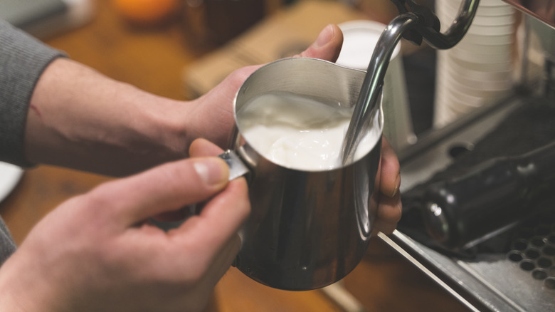 person holding cup under milk frother