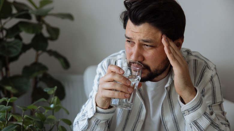 Man with headache drinks water