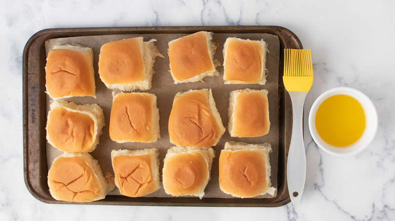 Rolls on baking sheet with pastry brush and bowl of melted