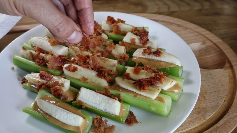 adding crumbled bacon to ants on a log