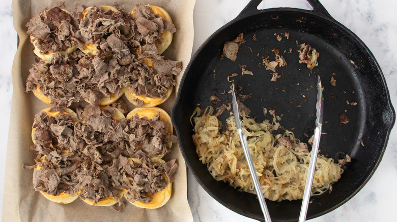 Slider rolls with sliced steak next to pan of cooked onions