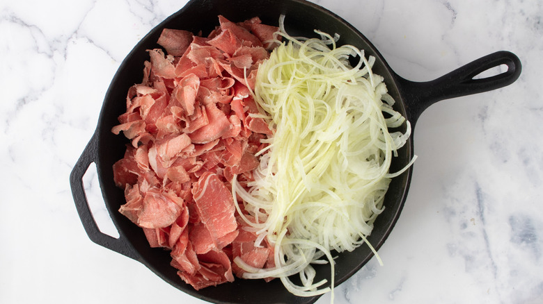 Raw meat and sliced onions in black frying pan