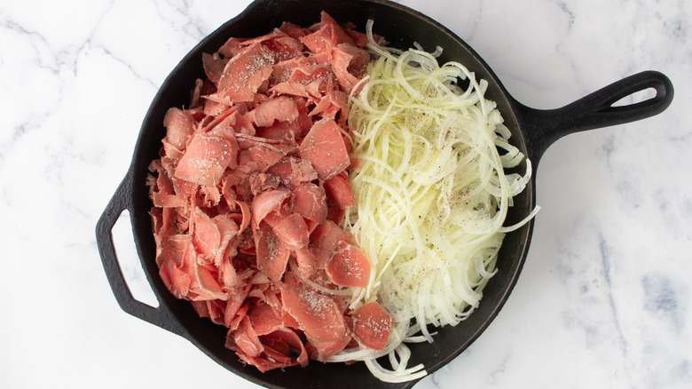 Raw meat and sliced onions in black frying pan