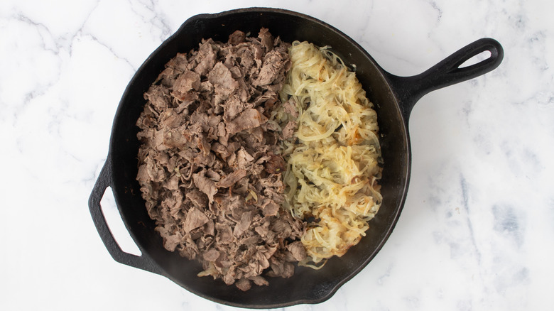 Cooked meat and sliced onions in black frying pan