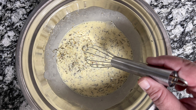 Hand whisking eggs, cream, and herbs in bowl