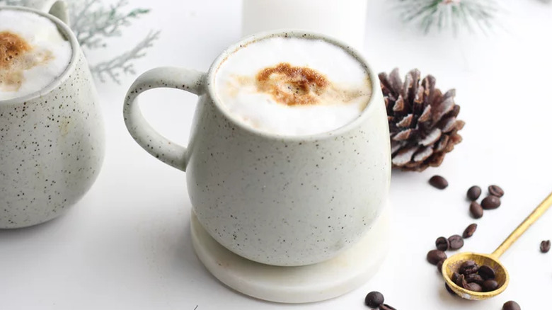 White mug with foam topped drink and coffee beans on table. 