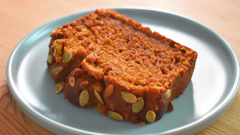 Slice of pumpkin bread with pumpkin seeds on plate.