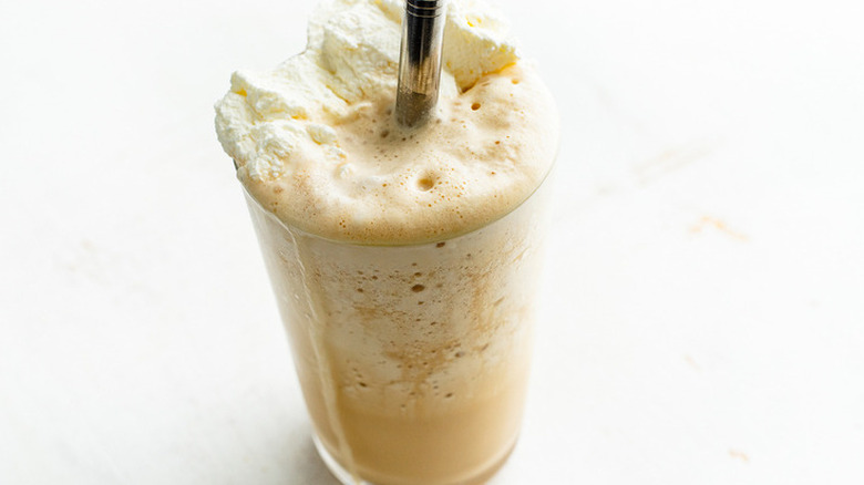 Glass of frothed milk and coffee drink with straw.