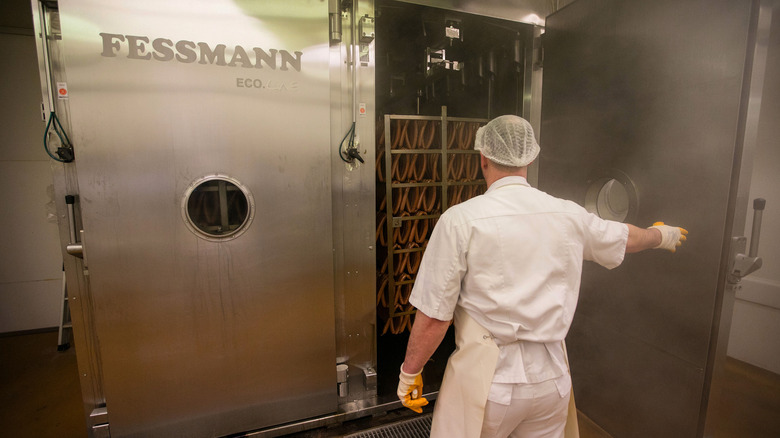 worker puts sausage in smoker