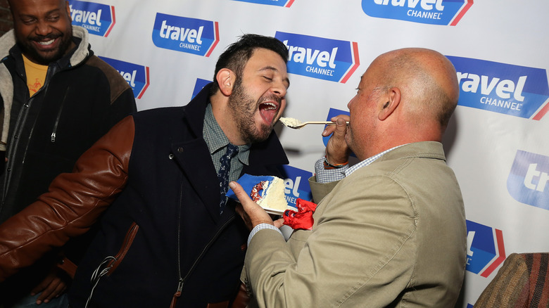 Andrew Zimmern feeding Adam Richman cake