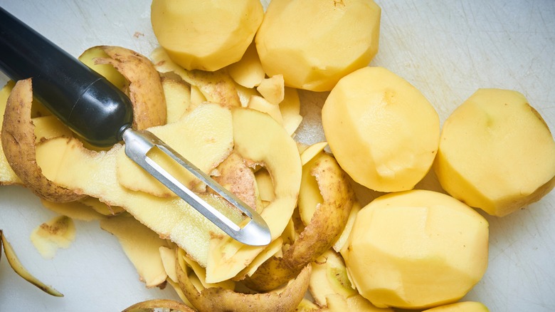 Peeled russet potatoes and peeler