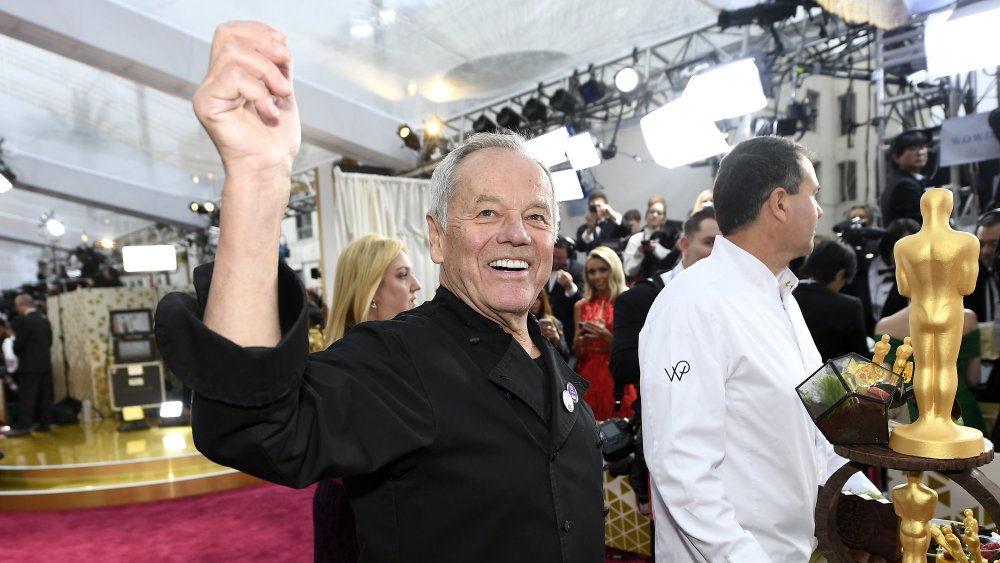 Wolfgang Puck at the Oscars raising his hand with wide smile