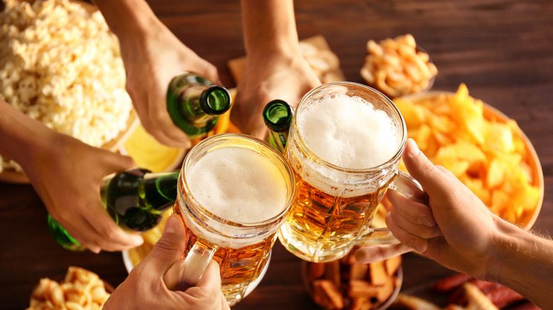 Bottles and mugs of beer clinking over popcorn and potato chips