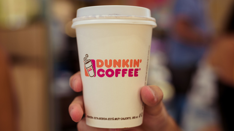 Hand holding paper cup of Dunkin' coffee