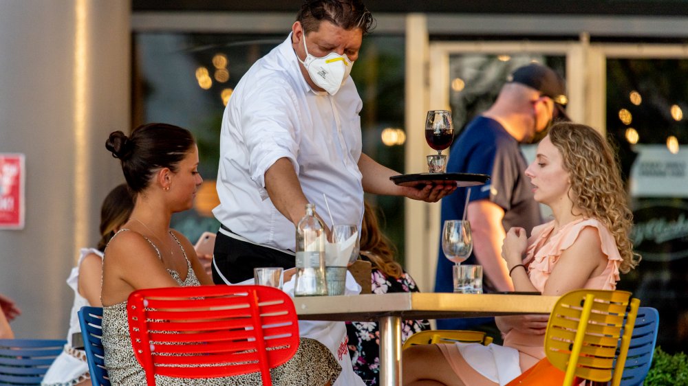 Waiter with face mask serving female customers