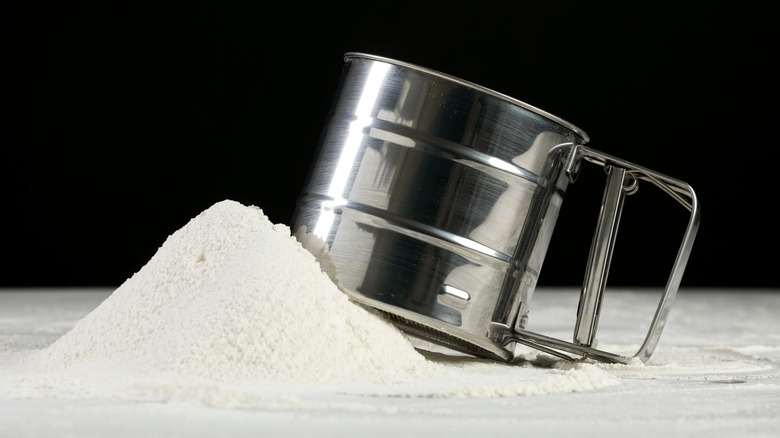 a flour sifter next to a pile of flour on a dark background