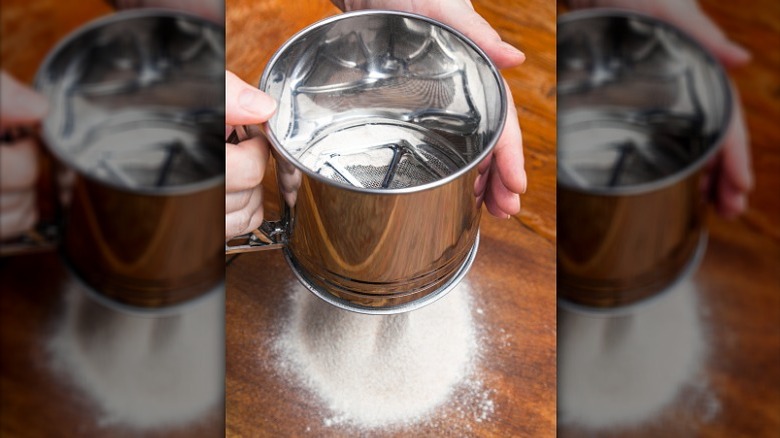 Person sifting flour into bowl with small sieve