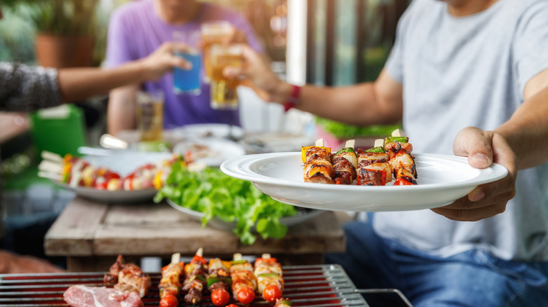 People toasting with drinks and passing plates of food at outside table