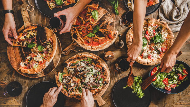 Top view of people grabbing slices from multiple pizzas 