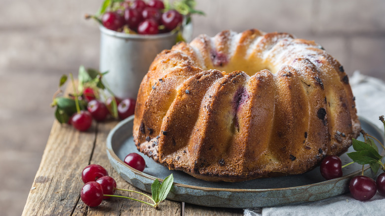 Bundt cake on metal slab surrounded by cherries