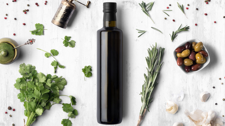 A dark bottle of olive oil surrounded by herbs and spices