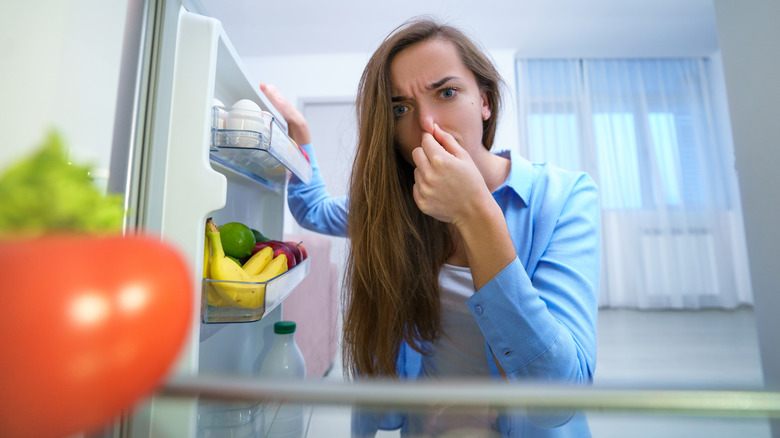 woman with hand over her nose at foul smell coming from open fridge