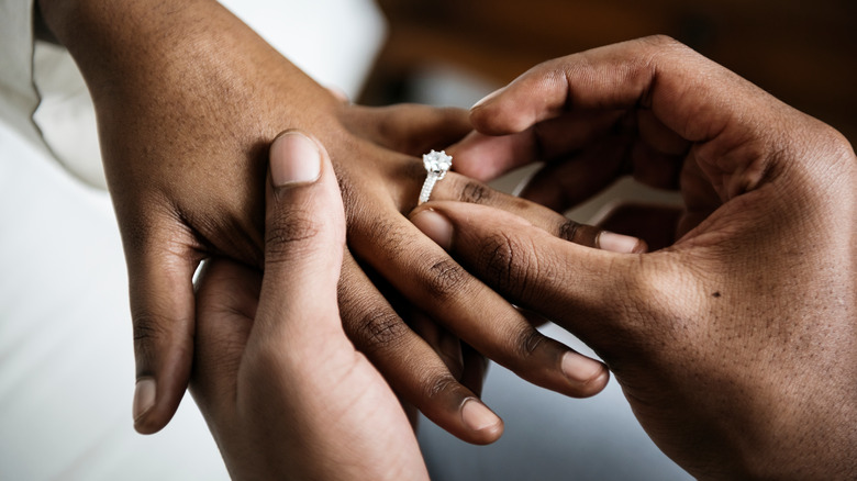 Man's hand placing an engagement ring on a woman's finger