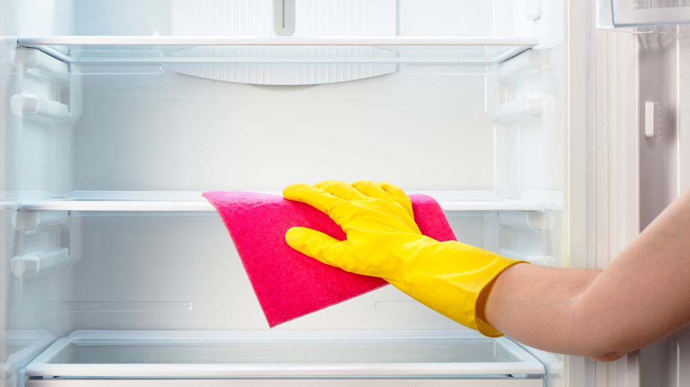 Gloved hand wiping down fridge shelves