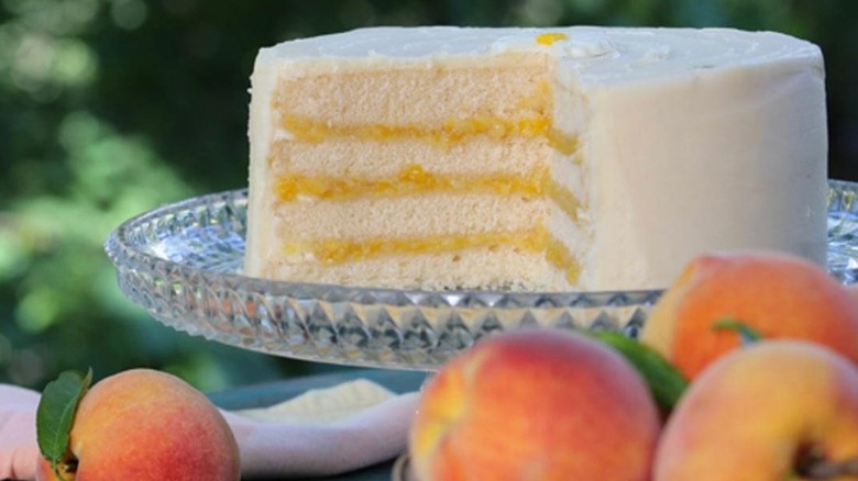 Daisy Cakes Peaches and Cream cake on a glass cake stand with whole peaches