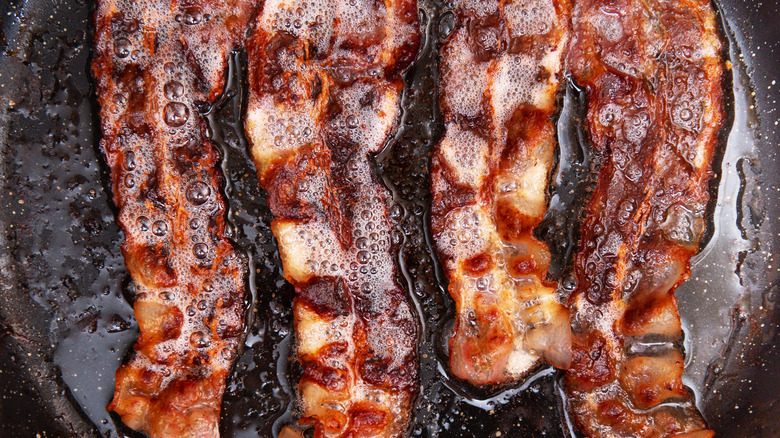 four slices of bacon cooking in a skillet