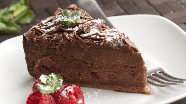 Slice of chocolate torte with raspberries on white plate with fork